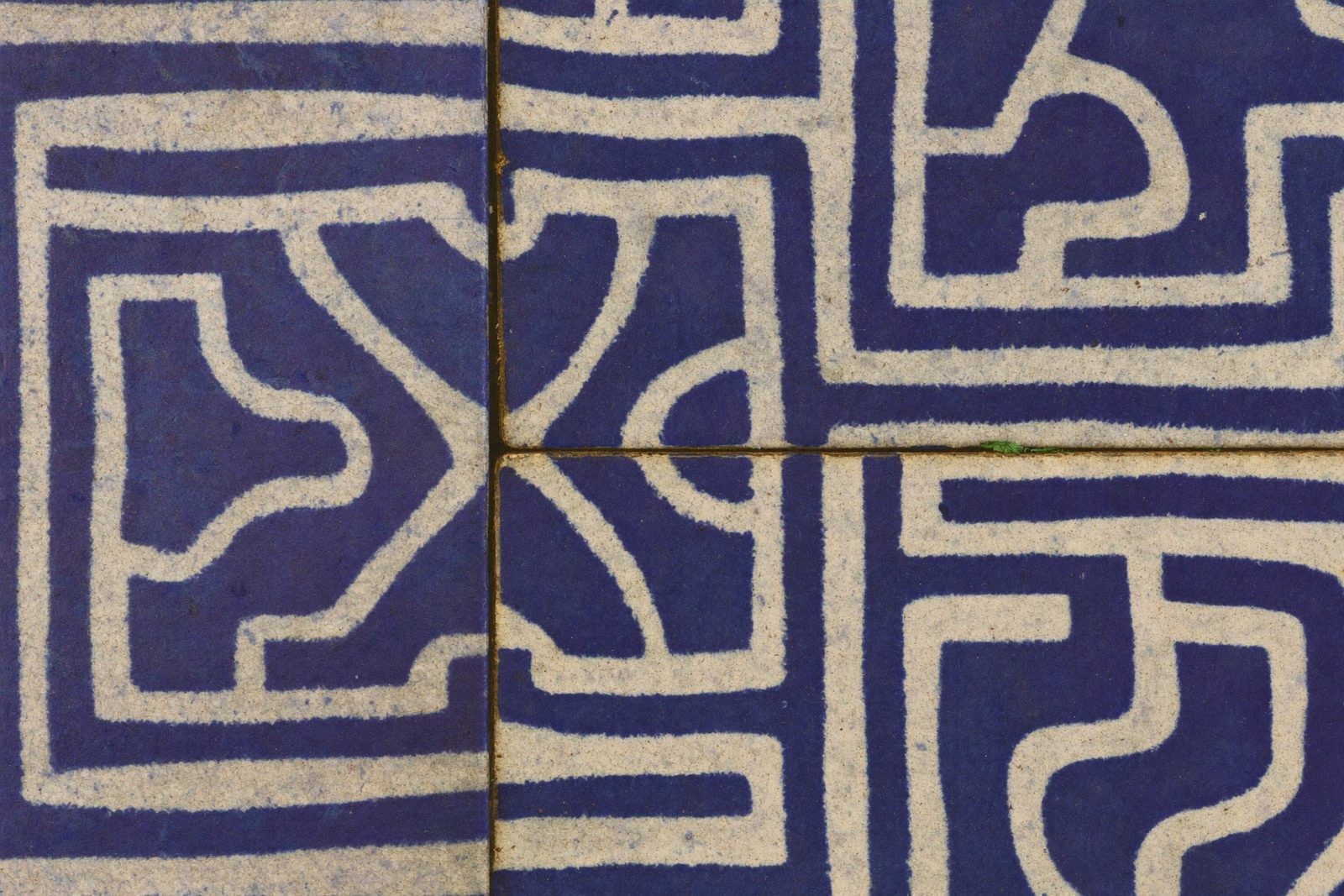 Zbliżenie na glazurowane kafle ceramiczne z geometrycznym wzorem Art Deco — niebieski i kremowy, widoczne spoiny i nierówności powierzchni szkliwa, starzejąca się ceramika