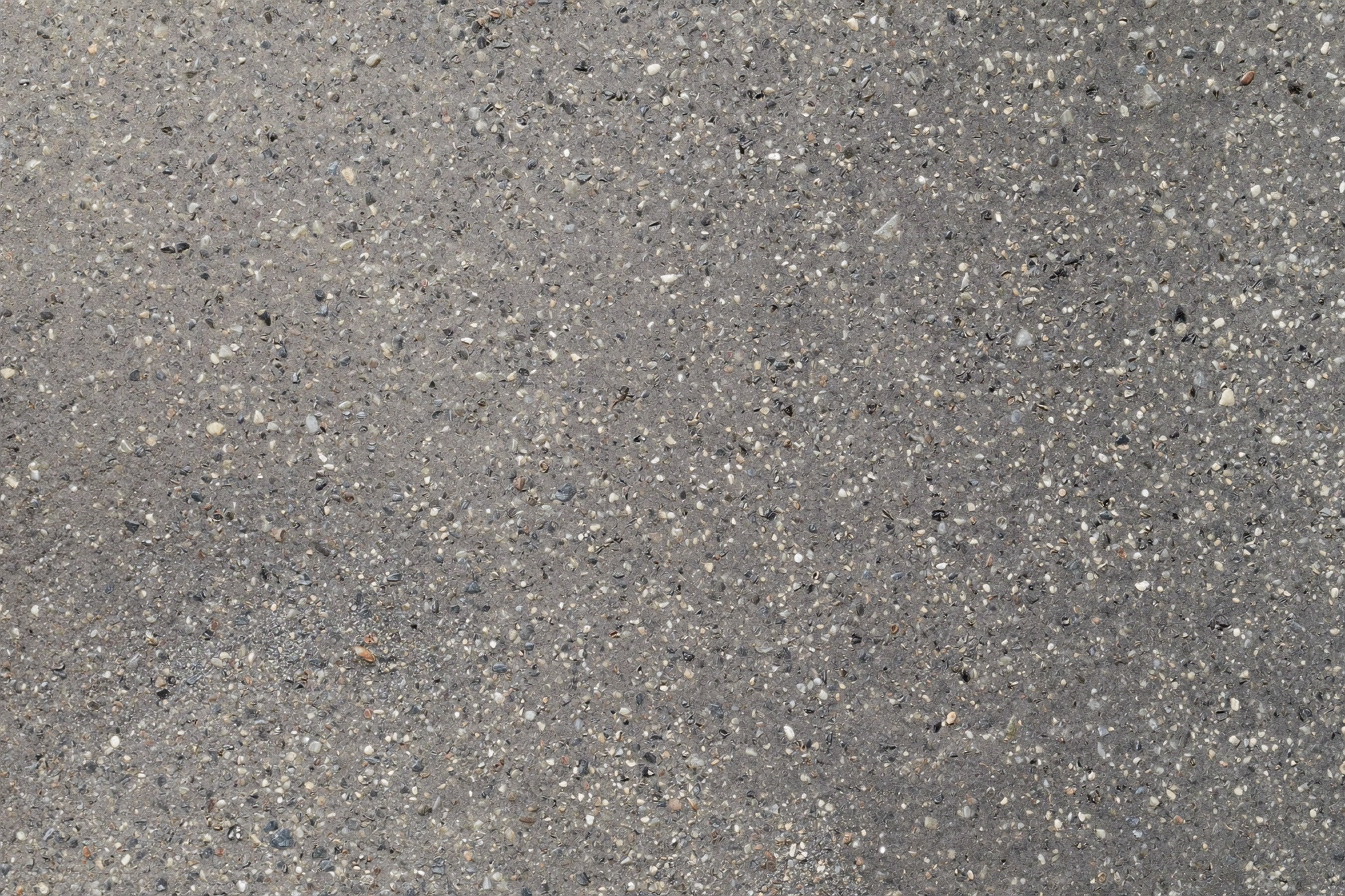 Zbliżenie betonu architektonicznego — drobiny kruszywa w cementowej osnowie, mikroskopijne pory po pęcherzykach powietrza, matowa bezodbiciowa faktura. Kolor i ziarnistość są wynikiem składu mieszanki i warunków dojrzewania — nie warstwy wykończeniowej. Wizualizacja: Higgsfield soul_2.
