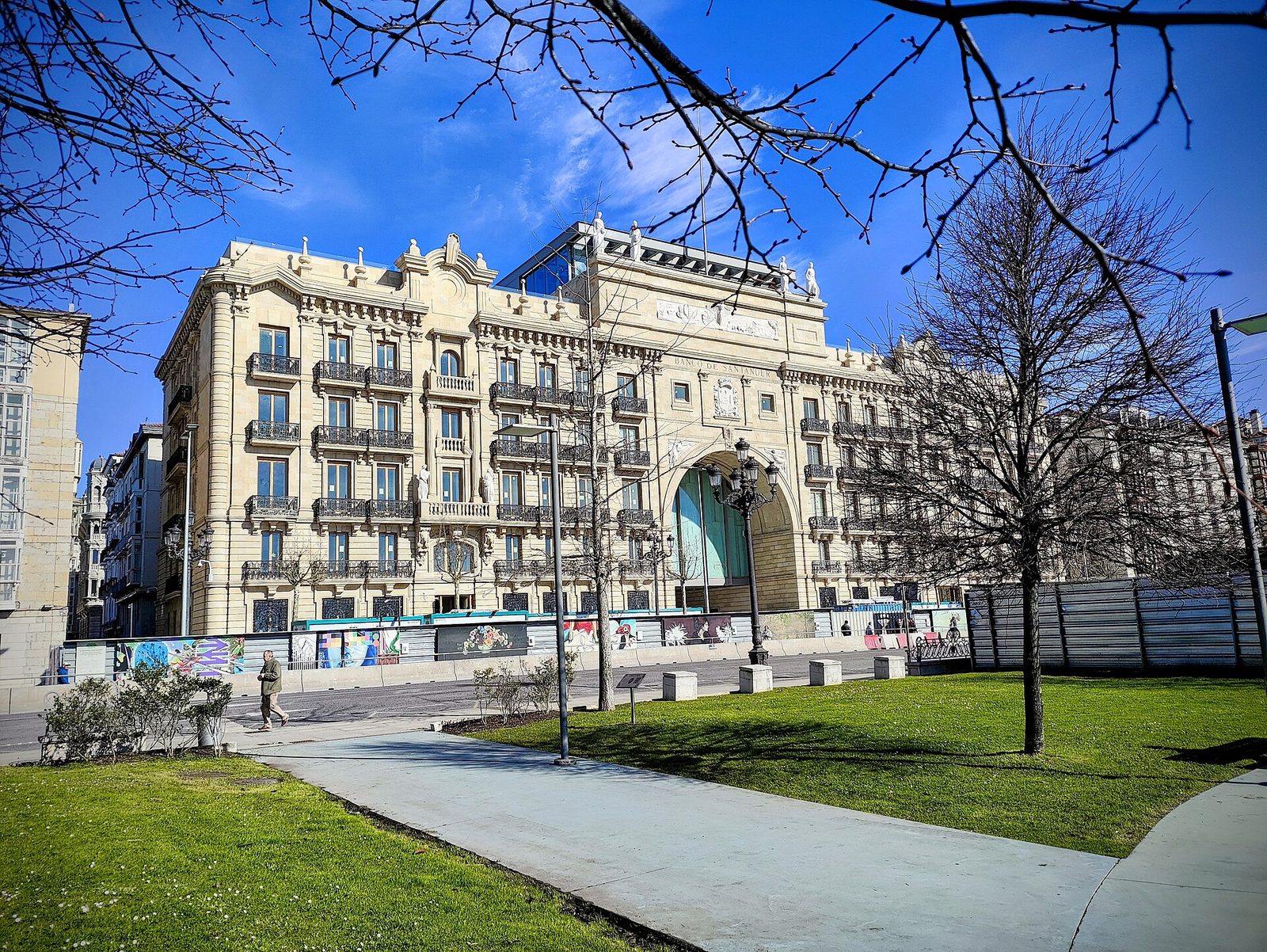Historyczna fasada Edificio Pereda w Santander — dawna siedziba Banco Santander, teraz Faro Santander — z nowoczesnym szklanym portalem wejściowym na tle błękitnego nieba. Fot. Emilio Gómez Fernández, CC BY-SA 4.0, Wikimedia Commons