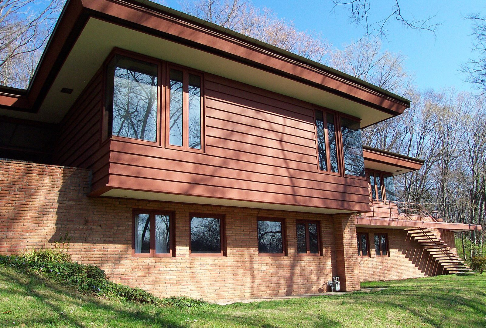 Modernistyczny dom z szerokim horyzontalnym okapem, ceglaną podstawą i drewnianą elewacją — widok zewnętrzny Usonian house w stylu Franka Lloyda Wrighta. Fot. Caustin021, CC BY-SA 4.0, Wikimedia Commons