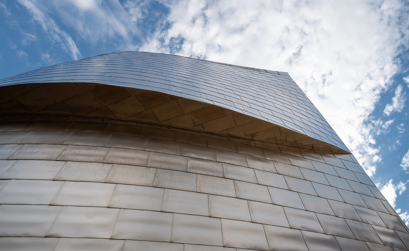 Zbliżenie na tytanową elewację Muzeum Guggenheima w Bilbao (Frank Gehry, 1997) — nieregularne panele ze stali tytanowej w miękkim świetle dziennym. Fot. Jules Verne Times Two, CC BY-SA 4.0, Wikimedia Commons