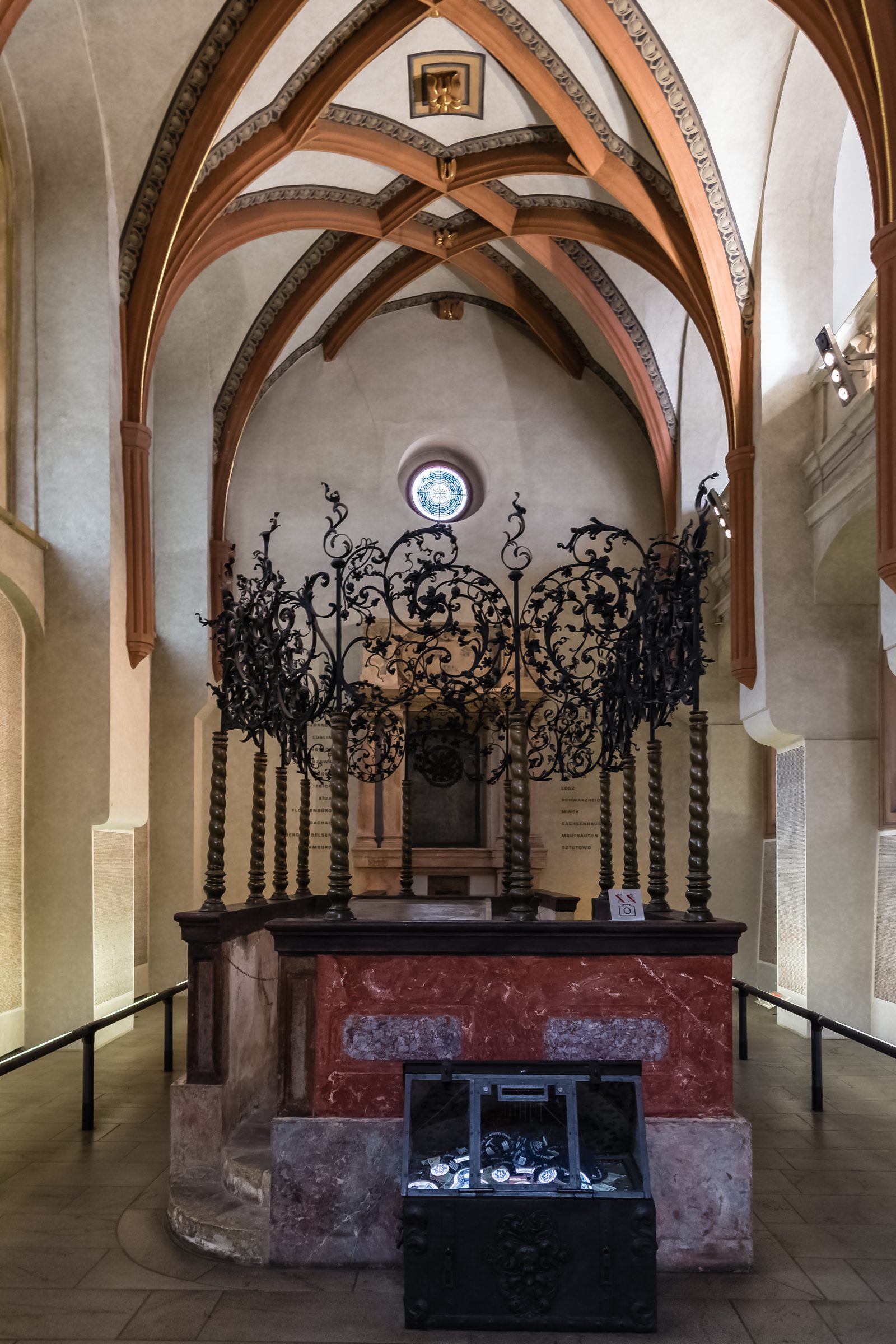 Wnętrze Starej Synagogi Pinkasa w Pradze — gotyckie sklepienie krzyżowo-żebrowe z tynkowanymi skoskami, czerwona marmurowa podstawa, puste wnętrze w miękkim bocznym świetle. Fot. Uoaei1, CC BY-SA 4.0, Wikimedia Commons