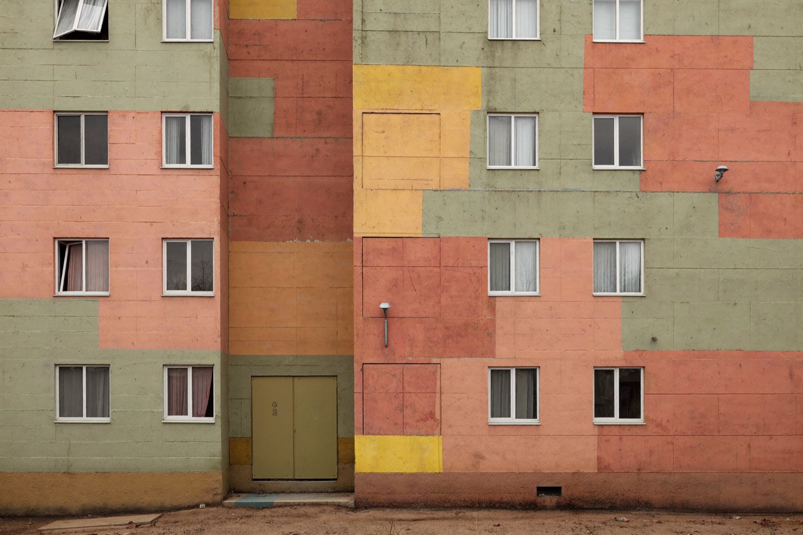 Ocieplony blok po remoncie: brzoskwiniowe, pistacjowe i cytrynowe pola tynku ułożone w geometryczne wzory